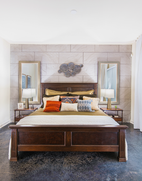 Model bedroom with wooden bedframe, concrete floors with two side mirrors behind night stands at MAA Stratford luxury apartments in Atlanta, GA