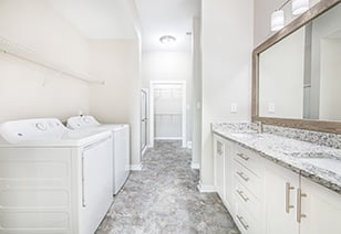 Modern bathroom with double sinks and large vanity mirror with granite countertops, white cabinets and washer and dryer at MAA Stratford luxury apartments in Atlanta, GA