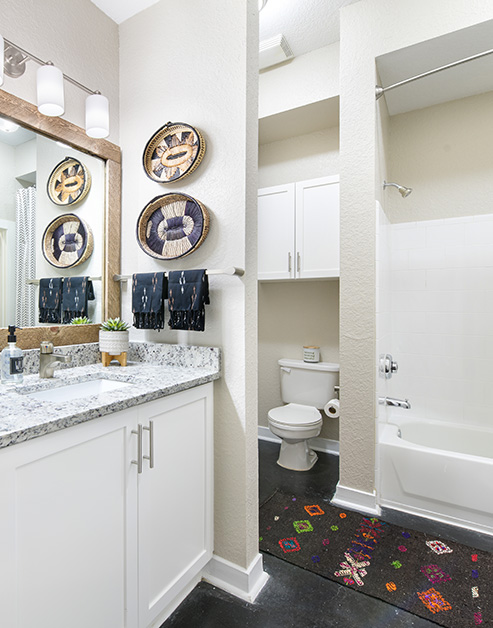Modern bathroom with framed vanity mirror above granite countertops, white cabinets next to a private toilet and shower on dark floors at MAA Stratford luxury apartments in Atlanta, GA