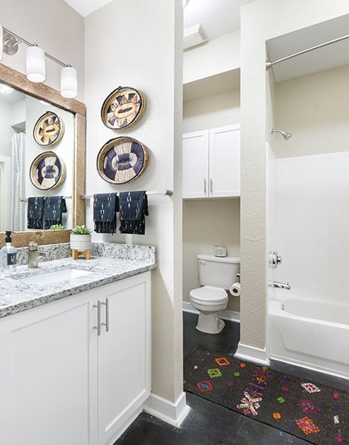 Modern bathroom with framed vanity mirror above granite countertops, white cabinets next to a private toilet and shower on dark floors at MAA Stratford luxury apartments in Atlanta, GA