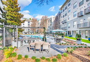 Poolside grilling station with patio tables and chairs surrounded by planters and trees situated next to the apartment complex at MAA Stratford luxury apartments in Atlanta, GA