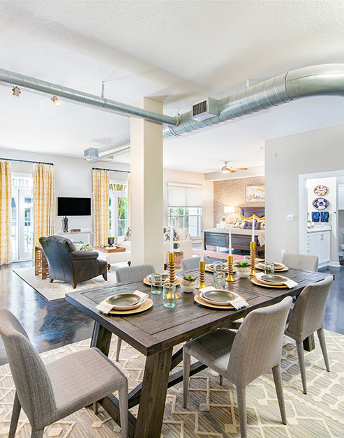 Open floorplan living room with exposed ceiling duct system, a sitting area with windows next to dining area with wood dining table and chairs on concrete floors at MAA Stratford luxury apartments in Atlanta, GA