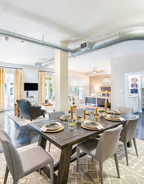 Open floorplan living room with exposed ceiling duct system, a sitting area with windows next to dining area with wood dining table and chairs on concrete floors at MAA Stratford luxury apartments in Atlanta, GA