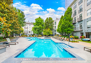 Long view of resort-style pool with lounge chairs surrounded by lush trees situated next to the apartment complex at MAA Stratford luxury apartments in Atlanta, GA