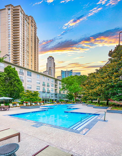 Resort-style pool with lounge chairs surrounded by lush trees and potted flowers situated next to the apartment complex at MAA Stratford luxury apartments in Atlanta, GA