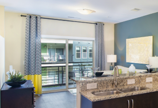 Living room view of sliding glass doors with open curtains to a balcony view situated next to kitchen bar top counter at MAA 1225 luxury apartments in Charlotte, NC