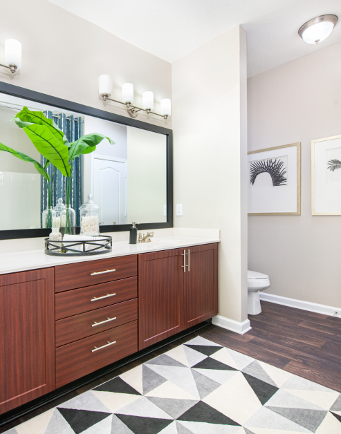 Upscale modern bathroom with large framed vanity mirror, white countertop with brown cabinets and area rug on dark wood floors at MAA Ballantyne luxury apartments in Charlotte, NC