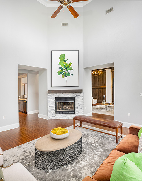 Community clubhouse with vaulted ceiling and a ceiling fan with a large wall painting over fireplace next to sitting area on hard wood floors at MAA Beverly Crest luxury apartments in Charlotte, NC