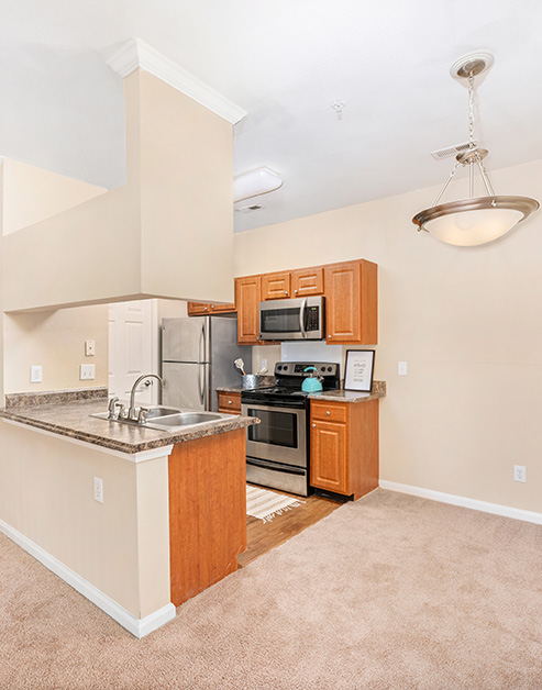 Modern-style open kitchen with wood cabinets, stainless steel appliances, double sink on granite bartop counter next to empty dining area at MAA Beverly Crest luxury apartments in Charlotte, NC