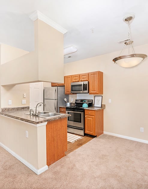 Modern-style open kitchen with wood cabinets, stainless steel appliances, double sink on granite bartop counter next to empty dining area at MAA Beverly Crest luxury apartments in Charlotte, NC