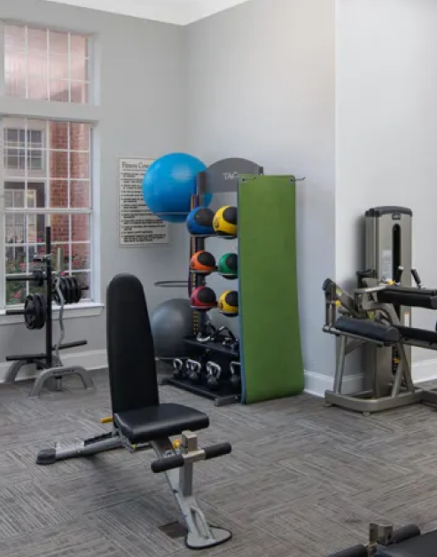 Fitness center with gym equipment and exercise ball racks next to large window with carpet flooring at MAA Beverly Crest luxury apartments in Charlotte, NC