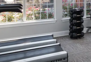 Close up view of fitness center treadmills and free weights rack next to large windows at MAA Beverly Crest luxury apartments in Charlotte, NC