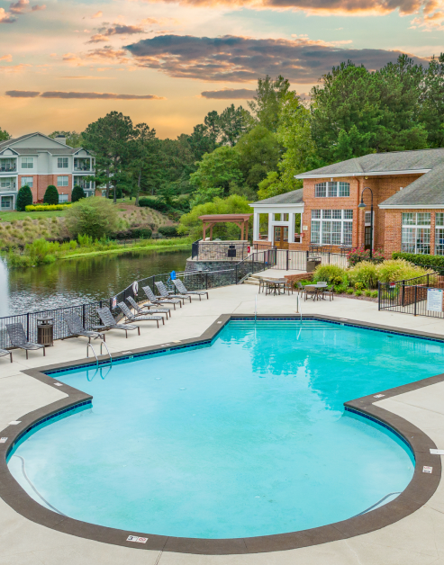 Aerial view of lakeside swimming pool area with lounge chairs and patio table with chairs with lush greenery at MAA Beverly Crest luxury apartments in Charlotte, NC