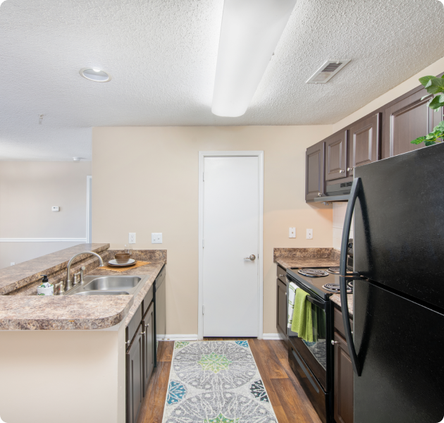 Apartment kitchen with dark brown cabinets, upgraded appliances and double sink on bar top counter with wood floors at MAA Chancellor Park luxury apartments in Charlotte, NC