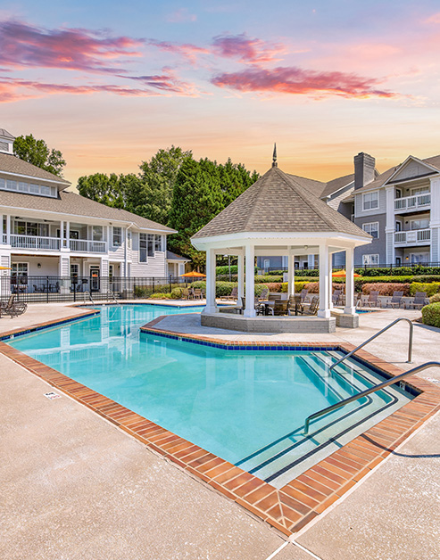 Long view of resort-style pool with entrance steps and metal handrails, a gazebo situated in the pool center, next to the apartment complex at MAA Chancellor Park luxury apartments in Charlotte, NC