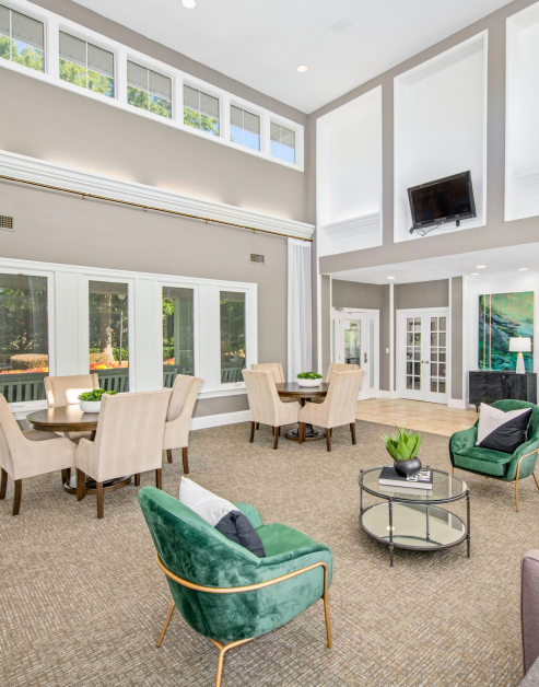 Community clubhouse main room with vaulted ceiling and high windows, wall mounted TV and multiple seating areas next to large windows at MAA Chancellor Park luxury apartments in Charlotte, NC