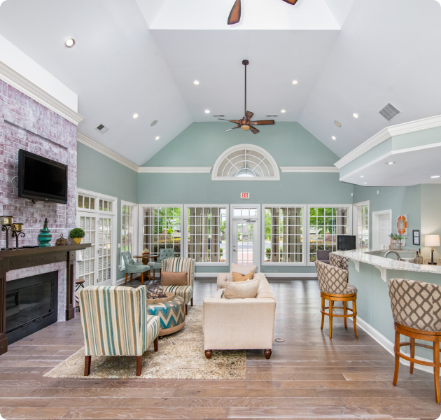 Community clubhouse with vaulted ceiling and ceiling fans, multiple seating areas next to the coffee bar and fireplace with large windows at MAA City Grand luxury apartments in Charlotte, NC