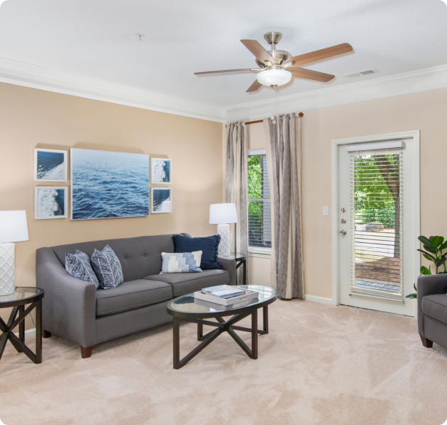 An apartment model living room with stylish couch and round coffee table, window with curtains next to French door with natural lighting at MAA Cornelius luxury apartments in Cornelius, NC