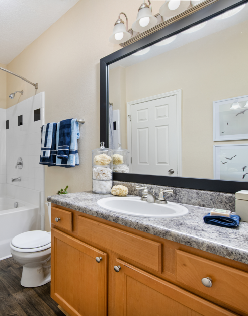 Bathroom with a large framed vanity mirror, granite countertop with sink and brown cabinets and dark wood floors at MAA Cornelius luxury apartments in Cornelius, NC