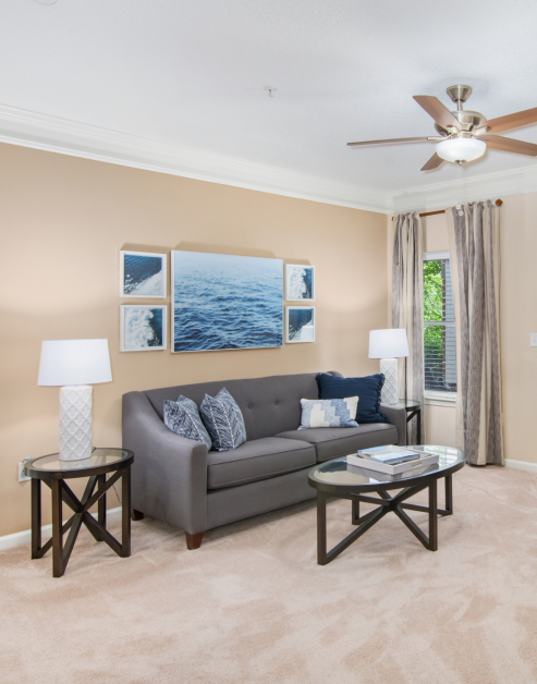 Model living room with wall paintings and a grey couch with round coffee table and curtains at MAA Cornelius luxury apartments in Cornelius, NC