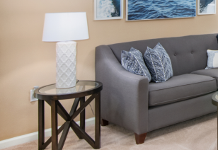 Close up view of grey couch in living room with glass top wooden side table and lamp at MAA Cornelius luxury apartments in Cornelius, NC