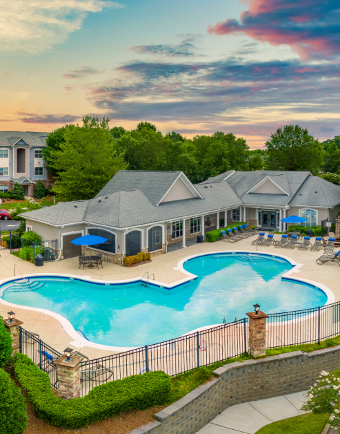 Aerial view of gated resort-style swimming pool with lounge chairs next to community center at MAA Cornelius luxury apartments in Cornelius, NC