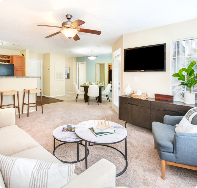 Apartment with carpeted large open space living and dining area with ceiling fan, TV unit next to the couch at MAA Fifty-One luxury apartments in Matthews, NC