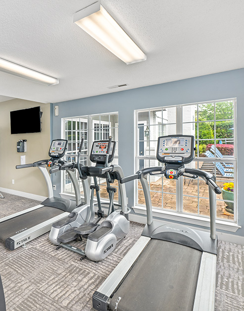 Fitness center with treadmills and workout machines in natural light next to large windows at MAA Fifty-One luxury apartments in Matthews, NC