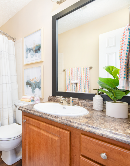 Close-up view of modern-style bathroom with a single sink and large vanity mirror on granite countertop with brown cabinets at MAA Fifty-One luxury apartments in Matthews, NC