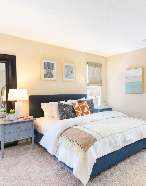 Model bedroom with light toned wall with art, white bedding with accent pillows and night stands at MAA Fifty-One luxury apartments in Matthews, NC