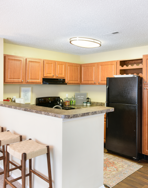 Stylish modern kitchen with brown cabinets, granite bar top counter with stools and upgraded appliances at MAA Fifty-One luxury apartments in Matthews, NC