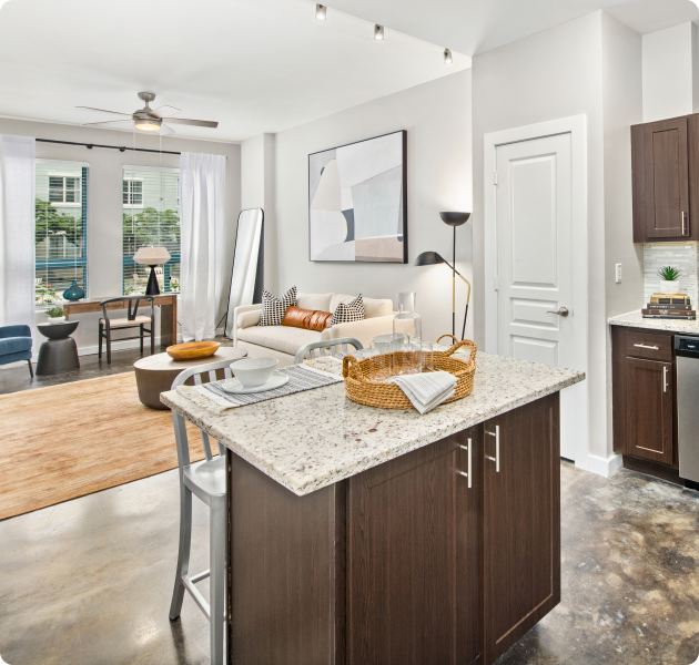 Apartment kitchen with track light fixtures and kitchen island countertop with chairs next to open living room area with ceiling fan, wall paintings and multiple sitting areas at MAA Gateway luxury apartments in Charlotte, NC
