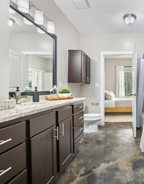 Modern design en suite bathroom with sleek light fixtures above large framed vanity mirror, single sink and light countertop with dark brown cabinets at MAA Gateway luxury apartments in Charlotte, NC