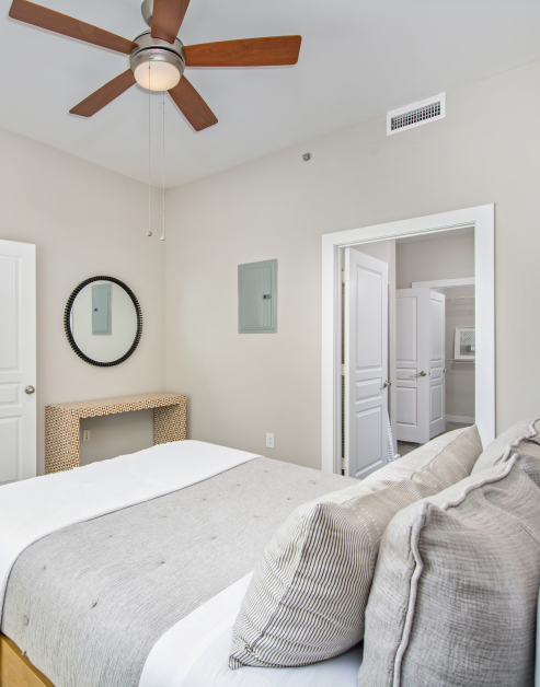 Bedroom with ceiling fan above a bed with accent pillows, wall mounted round mirror above nightstand with en suite bathroom at MAA Gateway luxury apartments in Charlotte, NC