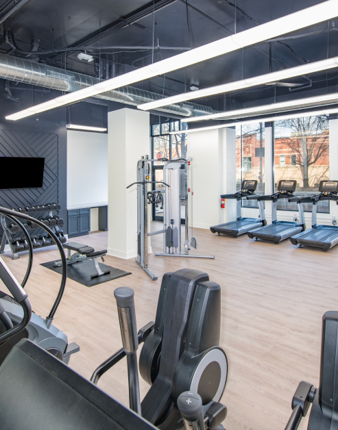 Industrial-style fitness center with wooden floors and variety of workout equipment next to large picture windows at MAA Gateway luxury apartments in Charlotte, NC
