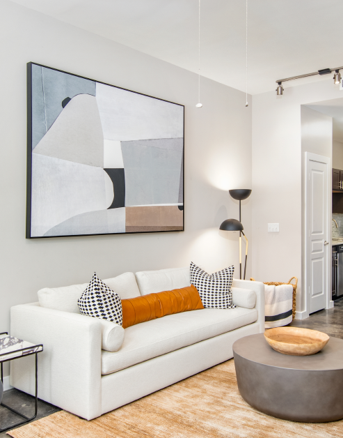 Living room with large abstract wall painting above white couch and dark gray round coffee table on an area rug at MAA Gateway luxury apartments in Charlotte, NC