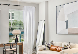 Living room wall painting above white couch and wooden desk lamp next to a large window with blinds and curtains at MAA Gateway luxury apartments in Charlotte, NC