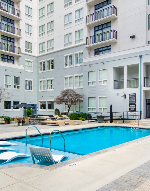 Swimming pool with sundeck loungers surrounded by lounge chairs, sun umbrella with patio table and chairs situated in the center courtyard of the apartment complex at MAA Gateway luxury apartments in Charlotte, NC