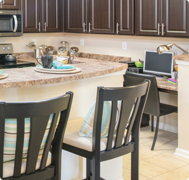 Close up of an apartment kitchen with dark brown cabinets, upgraded appliances and granite bartop counters with bartop chairs at MAA Huntersville luxury apartments in Huntersville, NC