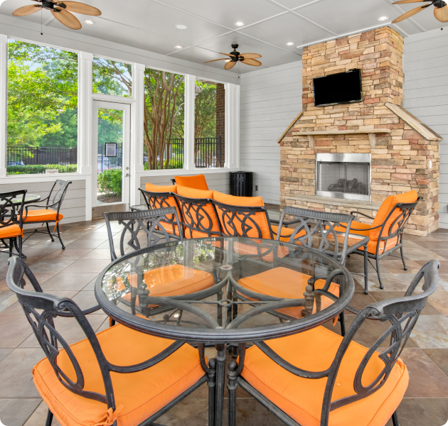 Community screened veranda lounge area with orange cushioned sitting areas, wall-mounted TV on a brick stone fireplace at MAA Huntersville luxury apartments in Huntersville, NC
