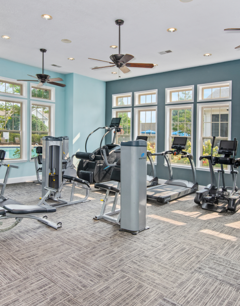 Fitness center with ceiling fans, modern treadmills and other workout machines in natural light next to large windows at MAA Huntersville luxury apartments in Huntersville, NC
