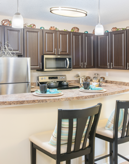 Modern kitchen with dark brown cabinets, stainless steel appliances and bartop granite counters with bartop chairs at MAA Huntersville luxury apartments in Huntersville, NC