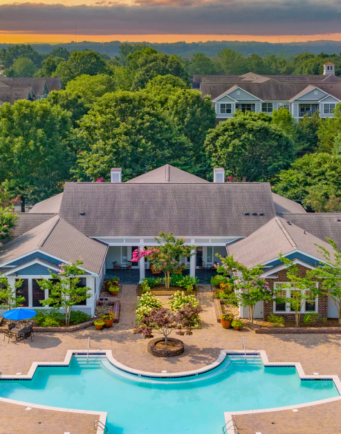 Resort-style swimming pool surrounded by lush trees situated next to the community clubhouse at MAA Huntersville luxury apartments in Huntersville, NC