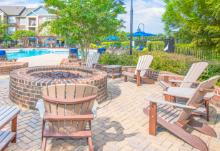 Poolside brick firepit surrounded by lounge chairs and lush greenery at MAA Huntersville luxury apartments in Huntersville, NC
