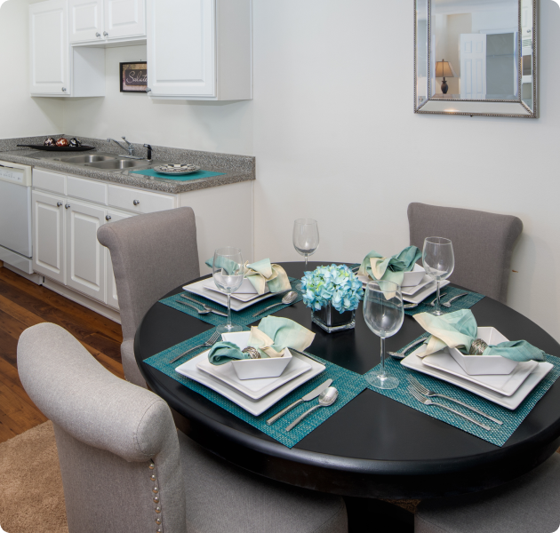 Apartment kitchen area with dining table and chairs, white cabinets and granite countertop with wood flooring at MAA Legacy Park luxury apartments in Charlotte, NC