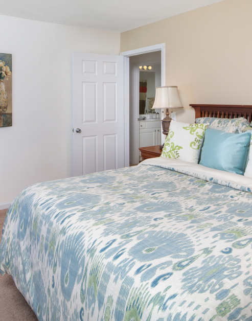 Master bedroom with a bed and accent pillows, bedside table lamp and en suite bathroom at MAA Legacy Park luxury apartments in Charlotte, NC