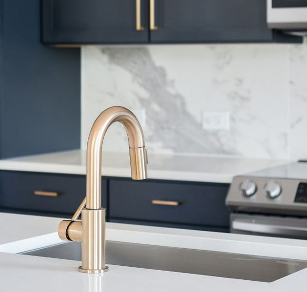A close up of a modern-style apartment kitchen with pristine white countertop and a brass modern sink faucet at MAA LoSo luxury apartments in Charlotte, NC