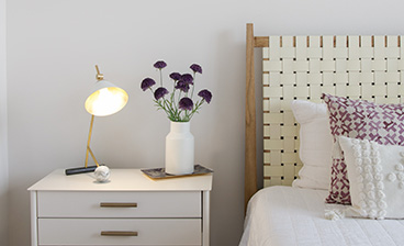 Close view of bedroom white nightstand with drawers and table lamp next to a bed with accent pillows at MAA LoSo luxury apartments in Charlotte, NC