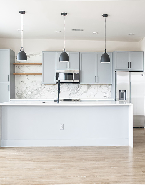 Modern-style kitchen with a marble white backsplash and hanging light fixtures over white countertop, light gray toned cabinets with stainless-steel appliances and wood floors at MAA LoSo luxury apartments in Charlotte, NC