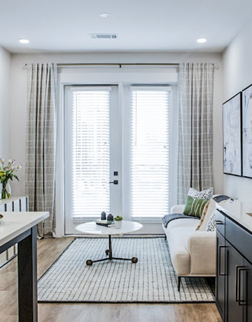 Living room with wood floors and round coffee table on area rug with double French doors with blinds and curtains at MAA LoSo luxury apartments in Charlotte, NC